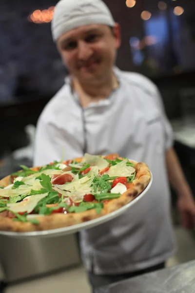 Retrato de cozinheiro atraente feliz com uma pizza nas mãos — Fotografia de Stock