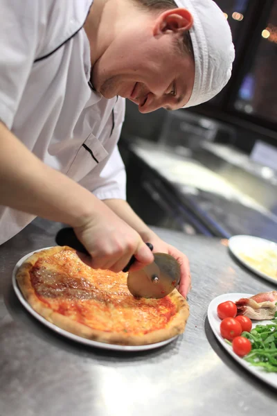 Gros plan main de chef boulanger en uniforme blanc coupe pizza à la cuisine Image En Vente