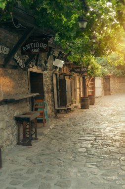 Bulgaristan 'ın tarihi Nessebar kentinde geleneksel taş binalar ve küçük hediyelik eşya dükkanlarıyla dolu sevimli, boş bir kaldırım taşı caddesi. Yeşil sarmaşıklar ve eski fenerler güneşli bir günde bu UNESCO Dünya Mirası sahasına kırsal bir atmosfer ekler..