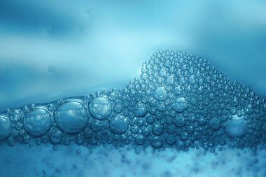 Canlı mavi su kabarcıkları ve köpüklerden oluşan makro çekim, tazelik, temizlik, hijyen, spa tedavileri veya bilimsel kavramların teması için soyut bir arkaplan oluşturur..