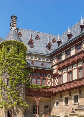 Almanya 'nın Harz kentindeki tarihi Wernigerode Kalesi avlusunun mimari detayları. Süslü, yarı ahşap cepheler, yemyeşil sarmaşık ve açık mavi gökyüzü altında geleneksel kayrak tavanlar..