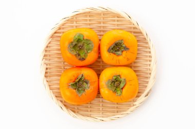 Kaki, beyaz arka planda bambu elek üzerine hurma meyvesi.