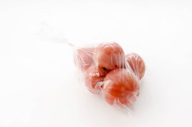 Beyaz arka planda plastik poşette olgun kırmızı domatesler.