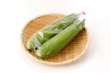 Taze yeşil sünger kabağı ya da beyaz arka planda bambu elek üzerinde plastik poşette luffa.