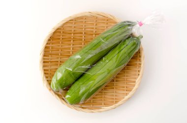 Taze yeşil sünger kabağı ya da beyaz arka planda bambu elek üzerinde plastik poşette luffa.