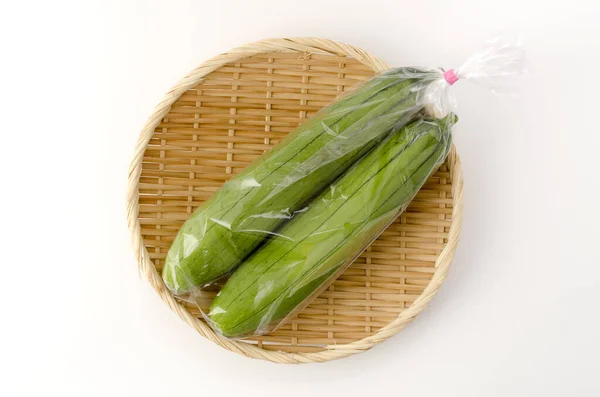 白色背景竹子筛子上的塑料袋中新鲜的绿色海绵葫芦或黄花菜 — 图库照片