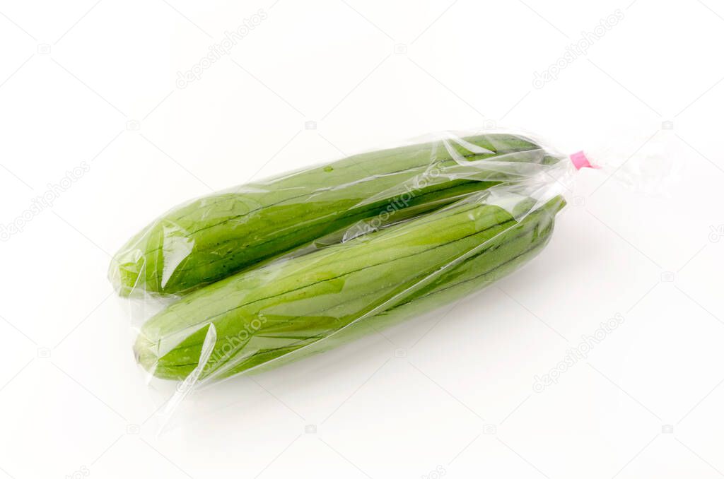 fresh green sponge gourd or luffa in plastic bag on white background