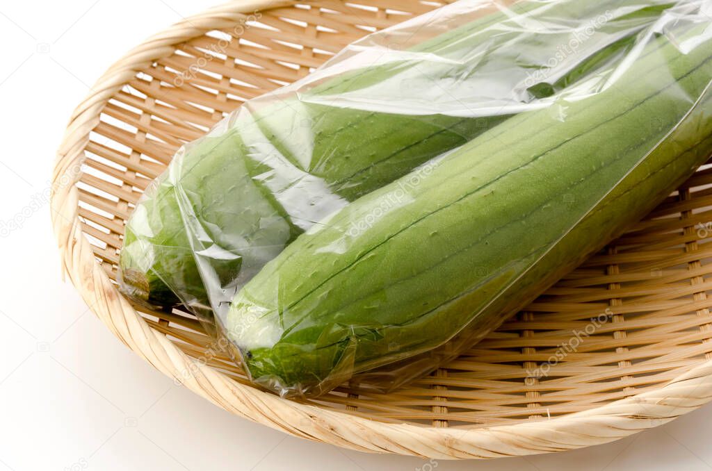 fresh green sponge gourd or luffa in plastic bag on a bamboo sieve on white background