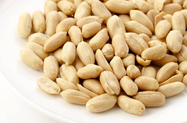 Beyaz arka planda beyaz bir tabakta kavrulmuş tuzlu fıstık.