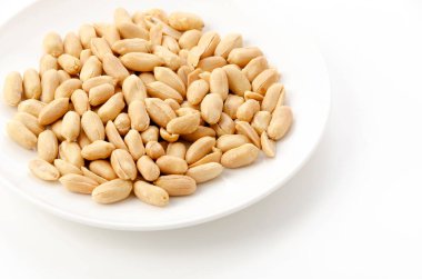 Beyaz arka planda beyaz bir tabakta kavrulmuş tuzlu fıstık.