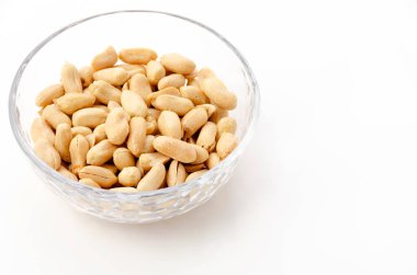 Beyaz arka planda şeffaf cam bir kasede kavrulmuş tuzlu fıstık.