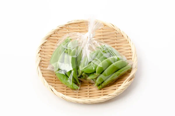 sugar snap pea in plastic bag on bamboo sieve on white background
