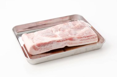 Çiğ donmuş domuz göbeği beyaz arka planda paslanmaz çelik tepside. 