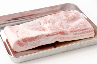 Çiğ donmuş domuz göbeği beyaz arka planda paslanmaz çelik tepside. 