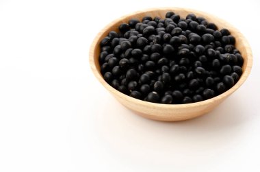 Beyaz arka planda, ahşap kasede pişmemiş siyah fasulyeler.