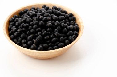 Beyaz arka planda, ahşap kasede pişmemiş siyah fasulyeler.