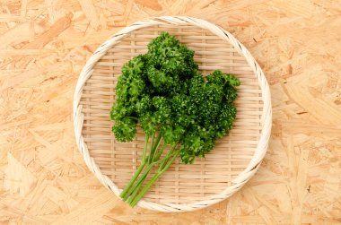 Tahta arka planda bambu elek üzerinde taze kıvırcık maydanoz.