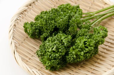 Beyaz arka planda bambu elek üzerine taze kıvırcık maydanoz.