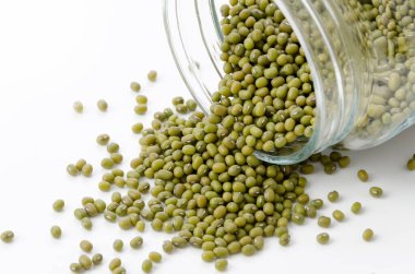 Mung fasulyeleri beyaz arka planda cam bir yemek kavanozundan dökülüyor.