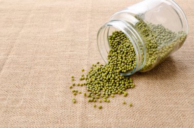 Mung fasulyeleri arka plandaki cam yemek kavanozundan dökülüyor.