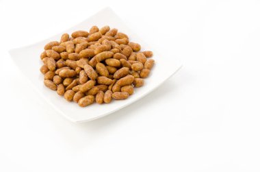 Beyaz arka planda beyaz bir tabakta kavrulmuş fıstık.
