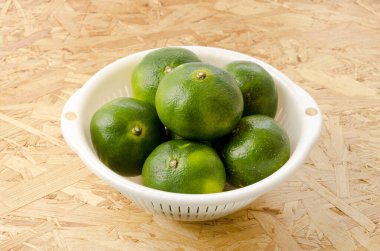 Citrus unshiu, mandarin satsuma portakalı, kontrplak tahta arka planda plastik kevgir.