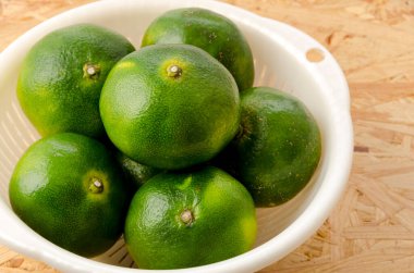 Citrus unshiu, mandarin satsuma portakalı, kontrplak tahta arka planda plastik kevgir.