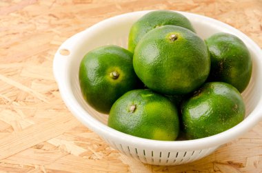 Citrus unshiu, mandarin satsuma portakalı, kontrplak tahta arka planda plastik kevgir.