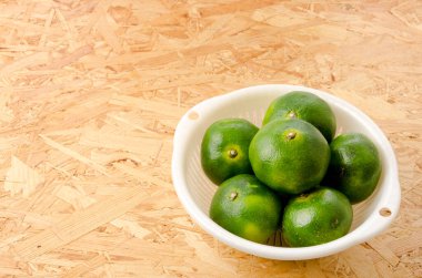 Citrus unshiu, mandarin satsuma portakalı, kontrplak tahta arka planda plastik kevgir.