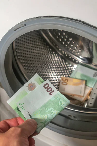 Money laundering concept, a man hand adding the 100 euro banknote into a pile of euro banknotes to be cleaned inside the washing machine, background, details