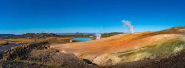 Panoramic view over geothermal active zones near Myvatn lake and Reykjahlid small town in Iceland, resembling Martian red planet landscape, at summer and blue sky. clipart