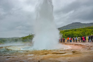 Geyser 'in panoramik manzarası, Güney İzlanda' da Geysir, Strokkur, Altın Daire 'de, yazın dramatik gökyüzü ve gayzerleri izleyen turistlerle