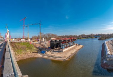 Almanya 'nın Magdeburg şehrinde, güneşli bir günde ve mavi gökyüzünde Elbe Nehri boyunca inşa edilecek yeni bir köprünün panoramik manzarası