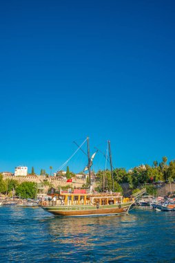 Antalya şehir merkezindeki Akdeniz sahili, plaj ve eski deniz manzarası ve geçmişten gelen bir korsan yelkenliye benzeyen büyük bir tur teknesi, Antalya, Türkiye.