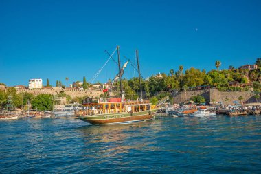Antalya şehir merkezindeki Akdeniz sahili, plaj ve eski deniz manzarası ve geçmişten gelen bir korsan yelkenliye benzeyen büyük bir tur teknesi, Antalya, Türkiye.