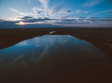 Ufukta orman ve şehir olan bir nehrin üzerinde gün batımı. Hava kararmak üzere..