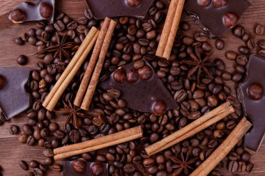 Kahve çekirdekleri ve baharatlarla ahşap bir masada fındıklı çikolata. Kavrulmuş kahve çekirdekleri, tarçın çubukları ve anason yıldızları. Üst görünüm.