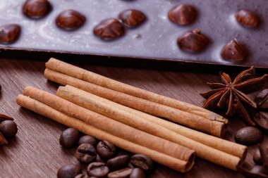 Kahve çekirdekleri ve baharatlarla ahşap bir masada fındıklı çikolata. Kavrulmuş kahve çekirdekleri, tarçın çubukları ve anason yıldızları. Fındıklı çikolata..