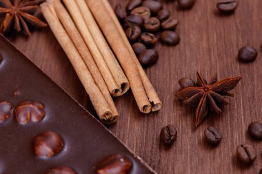 Kahve çekirdekleri ve baharatlarla ahşap bir masada fındıklı çikolata. Kavrulmuş kahve çekirdekleri, tarçın çubukları ve anason yıldızları. Fındıklı çikolata..