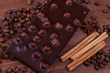 Kahve çekirdekleri ve baharatlarla ahşap bir masada fındıklı çikolata. Kavrulmuş kahve çekirdekleri, tarçın çubukları ve anason yıldızları. Fındıklı çikolata..