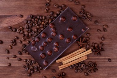 Kahve çekirdekleri ve baharatlarla ahşap bir masada fındıklı çikolata. Kavrulmuş kahve çekirdekleri, tarçın çubukları ve anason yıldızları. Fındıklı çikolata. Üst görünüm.