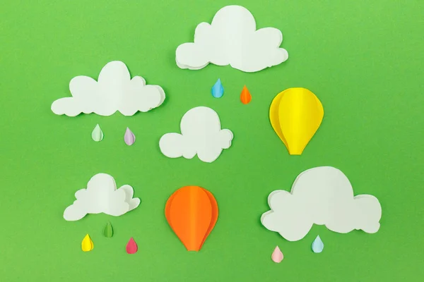 Cardboard clouds, raindrops and air balloons on the green background. Balloons in the sky with raindrops and clouds.