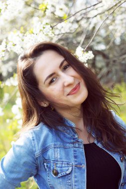 Bahar kızı portresi. Güzel esmer bir kızın açık hava portresi. Güneşli bir bahar gününde, çiçek açan kiraz ağacının yanındaki parkta gülümseyen bir kadın..