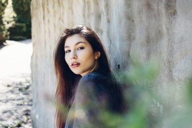 Güneşli bir günde beyaz beton duvarın önünde genç ve şık bir kızın portresi. Güzel bir kızın portresi. Uzun siyah saçlı ve kırmızı dudaklı güzel bir kız.. 