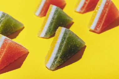 Sarı arka plana dizilmiş renkli üçgen jöle şekerler. Çok renkli marmelatlı reçelli şekerler. Macro, seçici odaklanma.