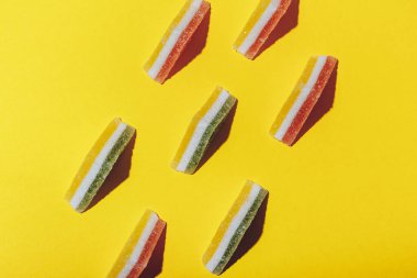 Sarı arka plana dizilmiş renkli üçgen jöle şekerler. Çok renkli marmelatlı reçelli şekerler. Üst görünüm.