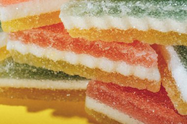 Çok renkli marmelatlı reçelli şekerler. Sarı arka planda üçgen marmelat şekeri yığını. Macro, seçici odaklanma.