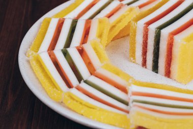 Ahşap arka plandaki tabakta dilimlenmiş çizgili marmelat. Renkli jöle şekerleri yakın plan. Makro çekim, seçici odaklanma.