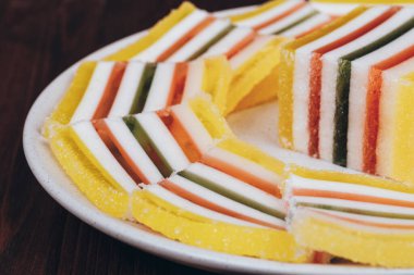 Ahşap arka plandaki tabakta dilimlenmiş çizgili marmelat. Renkli jöle şekerleri yakın plan. Makro çekim, seçici odaklanma.