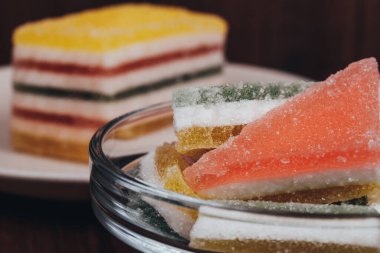 Colorful jelly candy in the plate and glass bowl on wooden background. Multi-colored marmalade jelly candy's. Heap of triangular and rectangular  marmalade candy. Macro shot, selective focus.